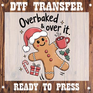May include: DTF transfer featuring a gingerbread man wearing a Santa hat and holding a mug. The text "Overbaked & over it" is above the gingerbread man. A candy cane and gift box are also included in the design. Ready to press.