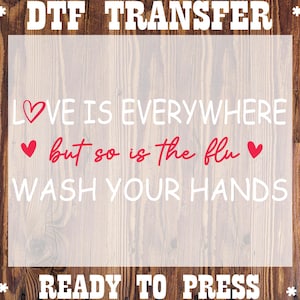 May include: A ready-to-press DTF transfer with the text "LOVE IS EVERYWHERE but so is the flu WASH YOUR HANDS". The words are in white and red, with heart symbols. The background is a wood grain.