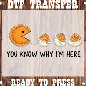 May include: DTF transfer design featuring a Pac-Man-like pie chasing three deviled eggs. The text "YOU KNOW WHY I'M HERE" is below the graphic, with "READY TO PRESS" at the bottom. The design is on a wood-grain background.