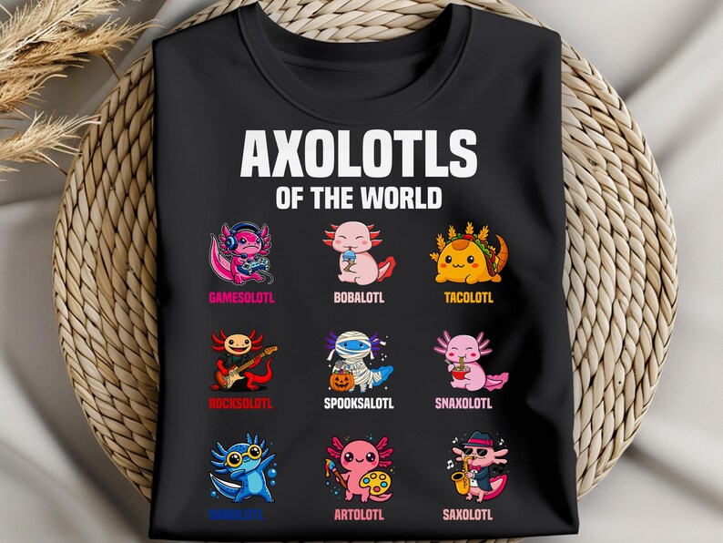 May include: Black t-shirt featuring the text "AXOLOTLS OF THE WORLD" above nine cartoon axolotl characters. Each axolotl is uniquely designed, with names like "GAMESOLOTL" and "TACOLOTL" below them. The shirt is displayed on a woven background.