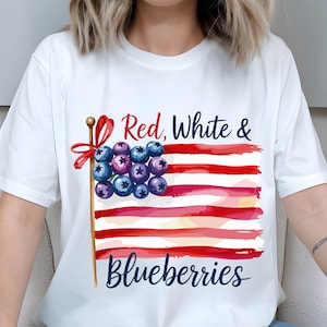 Könnte beinhalten: Weißes T-Shirt mit einem patriotischen Design. Die Grafik zeigt eine stilisierte amerikanische Flagge mit roten und weißen Streifen und Blaubeeren anstelle der Sterne. Der Text "Red, White & Blueberries" ist ebenfalls enthalten.