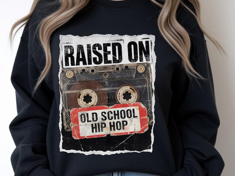 May include: Black sweatshirt featuring a graphic of a cassette tape with the words "RAISED ON" above and "OLD SCHOOL HIP HOP" below. The design has a distressed, vintage aesthetic.