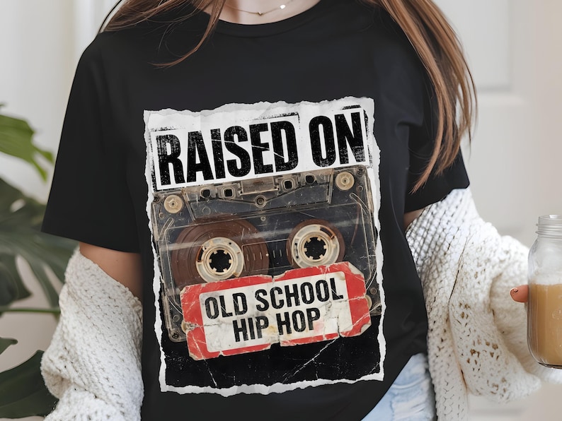 May include: Black t-shirt featuring a distressed graphic of a cassette tape with the words "RAISED ON" above and "OLD SCHOOL HIP HOP" below. The design is in white and red, evoking a vintage aesthetic.