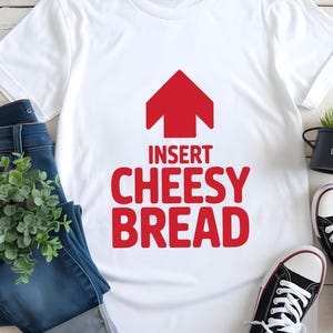 May include: White t-shirt with the text "INSERT CHEESY BREAD" in red, topped with a red arrow graphic. The shirt is paired with blue jeans, black sneakers, and a small potted plant, creating a casual, food-themed ensemble.