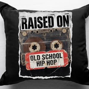 May include: Black square throw pillow featuring a vintage cassette tape design. The tape image has the words "RAISED ON" above and "OLD SCHOOL HIP HOP" below. The pillow is a decorative item.