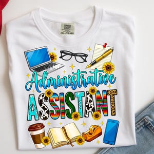 May include: White t-shirt with the words "Administrative Assistant" in a colorful design. The design includes a laptop, glasses, pen, sunflowers, coffee cup, book, tape dispenser, and a smartphone. The shirt is a Comfort Colors brand.