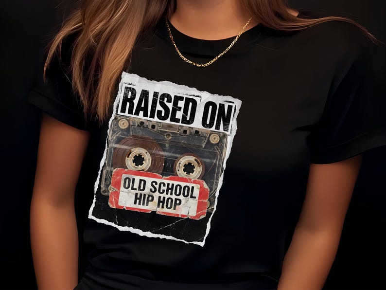May include: Black t-shirt featuring a cassette tape graphic with the words "RAISED ON OLD SCHOOL HIP HOP" in a distressed style. The design includes a vintage cassette tape image, evoking a retro music theme.