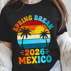 May include: Black t-shirt with a colorful graphic design. The design features the words "SPRING BREAK 2026 MEXICO" in a retro font, with a sunset and palm trees in the background. The shirt is a casual style.