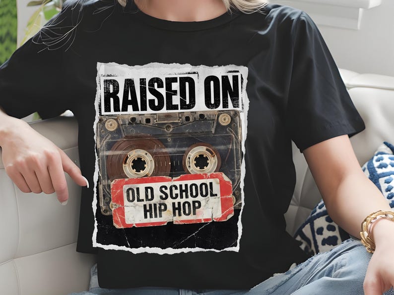 May include: Black t-shirt featuring a vintage cassette tape graphic. The design includes the text "RAISED ON" above the tape and "OLD SCHOOL HIP HOP" below, in a distressed style. The shirt is a classic crew neck.