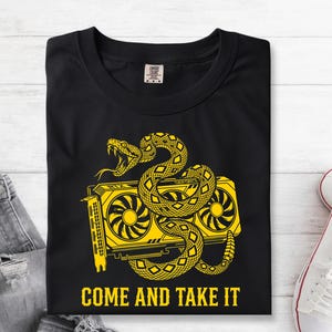 May include: A black t-shirt featuring a yellow graphic of a rattlesnake coiled around a computer graphics card. The text "COME AND TAKE IT" is printed in yellow capital letters below the illustration. The shirt has a crew neckline.