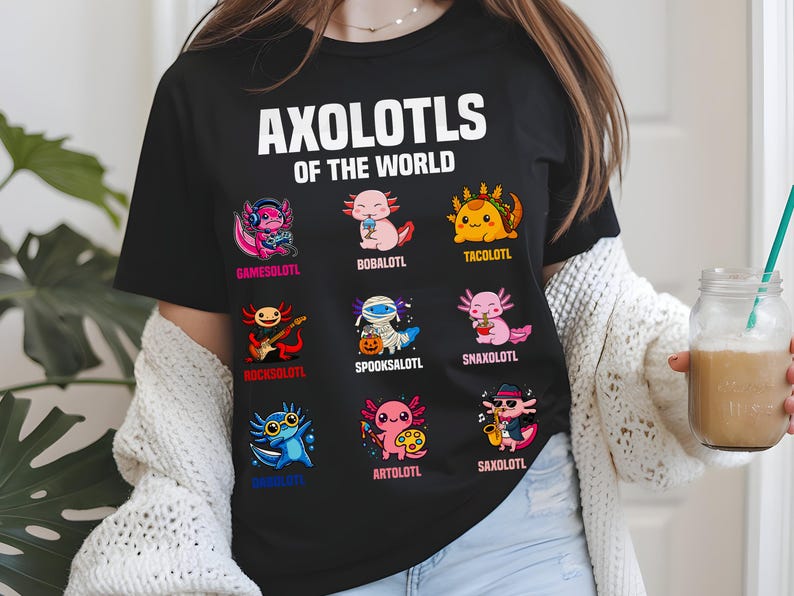 May include: Black t-shirt with the text "AXOLOTLS OF THE WORLD" above nine cartoon axolotl characters. Each axolotl is uniquely designed, including one with headphones, one as a taco, and one playing a guitar.