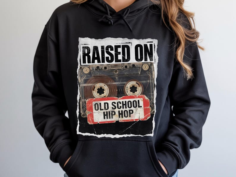 May include: Black hoodie featuring a graphic of a cassette tape with the words "RAISED ON" above and "OLD SCHOOL HIP HOP" below. The design has a vintage, distressed aesthetic, with a torn paper effect.