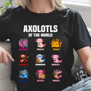 May include: Black t-shirt featuring the text "AXOLOTLS OF THE WORLD" above nine colorful axolotl illustrations. Each axolotl is uniquely designed, with names like "GAMESOLOTL" and "TACOLOTL" below them. The shirt is worn by a person.