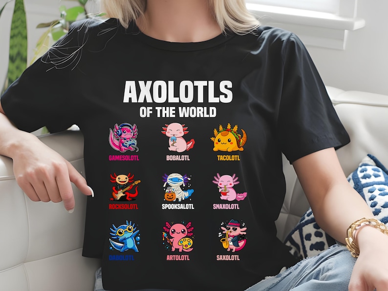 May include: Black t-shirt featuring the text "AXOLOTLS OF THE WORLD" above nine colorful axolotl illustrations. Each axolotl is uniquely designed, with names like "GAMESOLOTL" and "TACOLOTL" below them. The shirt is worn by a person.