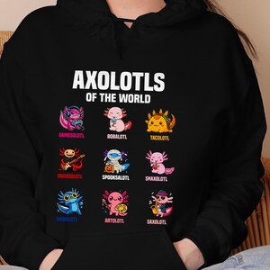 May include: Black hoodie featuring the text "AXOLOTLS OF THE WORLD" above nine cartoon axolotls, each with a unique design and name. The axolotls are in various colors and styles, including a gamer, a taco, and a musician.