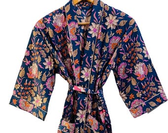 May include: A dark blue floral print robe with a matching belt. The robe features a vibrant pattern of pink, orange, and gold flowers and leaves. White trim accents the edges of the sleeves and front opening. The robe is hanging on a wooden hanger.