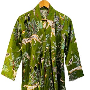 May include: A green, knee-length robe with a jungle-themed print. The robe features a repeating pattern of leopards, birds, and tropical foliage. The robe has long sleeves and a shawl collar, and is hanging on a wooden hanger.