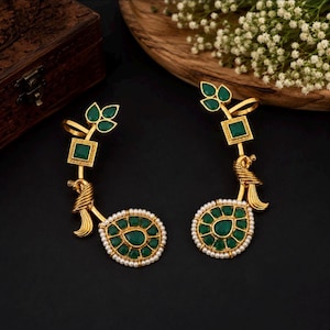 May include: A pair of gold-toned ear cuffs featuring green stones and white pearls. Each piece includes a leaf-shaped top, a square stone, a peacock-inspired motif, and a teardrop-shaped base surrounded by small white pearls in a gold setting.