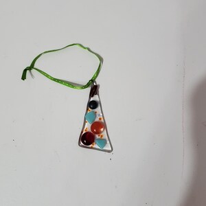 May include: A handmade pendant necklace with a triangular glass pendant. The pendant is outlined in silver and features colourful glass pieces in shades of blue, orange, and brown. It hangs from a green ribbon.