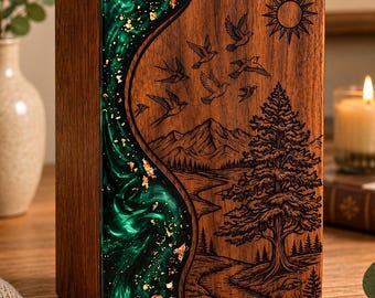 May include: A rectangular wooden cremation urn featuring a vertical, wavy inlay of swirling emerald green resin with gold leaf flakes. The wood surface is laser-engraved with a landscape of mountains, a pine tree, and birds.