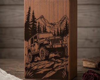 May include: A rectangular brown wooden block featuring a laser-engraved illustration of an off-road vehicle driving on a rocky path. The background depicts a dense forest of pine trees and tall mountain peaks, all rendered in dark brown tones.