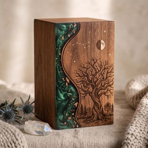 May include: A rectangular wooden urn featuring a dark walnut finish with a vertical, wavy inlay of emerald green resin infused with gold leaf flakes. The wood surface is laser-engraved with a detailed tree, a crescent moon, and a star constellation.