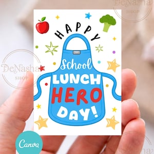 May include: A rectangular card with a blue apron design and the words "HAPPY SCHOOL LUNCH HERO DAY!" in a playful font. The card features illustrations of a red apple, broccoli, and stars. The card is held in a person's hand.