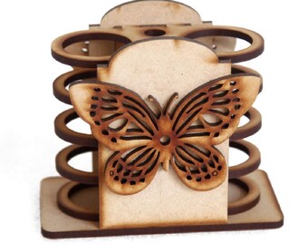 Puede incluir: Un organizador de escritorio de madera con un diseño de mariposa recortada. El organizador tiene una base rectangular, un panel central con una mariposa y varios compartimentos circulares. La madera es de color marrón claro natural.