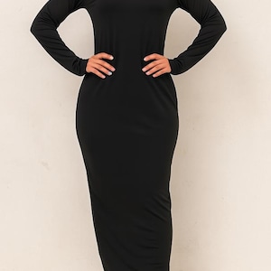 May include: A long, black, figure-hugging dress with long sleeves. The dress has a round neck and a floor-length hemline. The model is wearing black sandals. The dress is made of a soft, stretchy fabric.