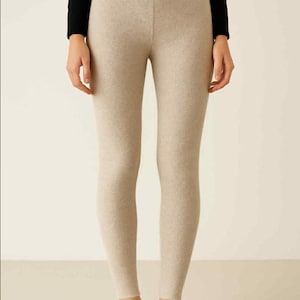 May include: Beige leggings with a ribbed waistband. The leggings are made of a soft material and are paired with black flats. The outfit is simple and comfortable, suitable for casual wear.