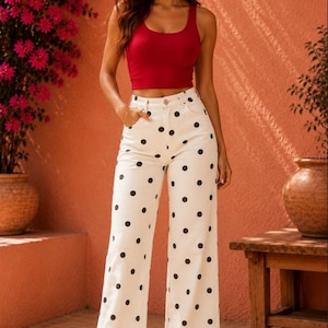 Peut inclure: Un haut court sans manches rouge associé à un pantalon blanc taille haute à jambes larges avec un motif à pois noirs. Le pantalon possède une fermeture à bouton et à glissière avec des poches avant. Le texte Bellachicvibes avec un cœur est visible.