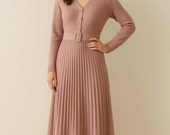 May include: A dusty rose-colored dress with a matching cardigan. The dress features a V-neck, long sleeves, a belted waist, and a pleated skirt. The model is wearing beige ankle boots. The dress is a midi length.