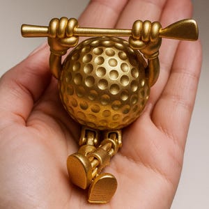 May include: A golden golf ball figurine with arms, legs, and a golf club. The golf ball has a dimpled surface and is holding the club above its head. The figurine is a decorative item.