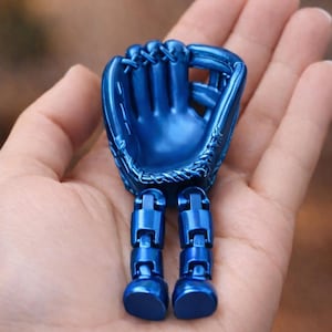 May include: A metallic blue baseball glove figurine with articulated legs. The glove is detailed with stitching and a webbed pocket. The legs are made of connected rectangular blocks, giving the figurine a unique, playful appearance. The figurine is held in a hand.