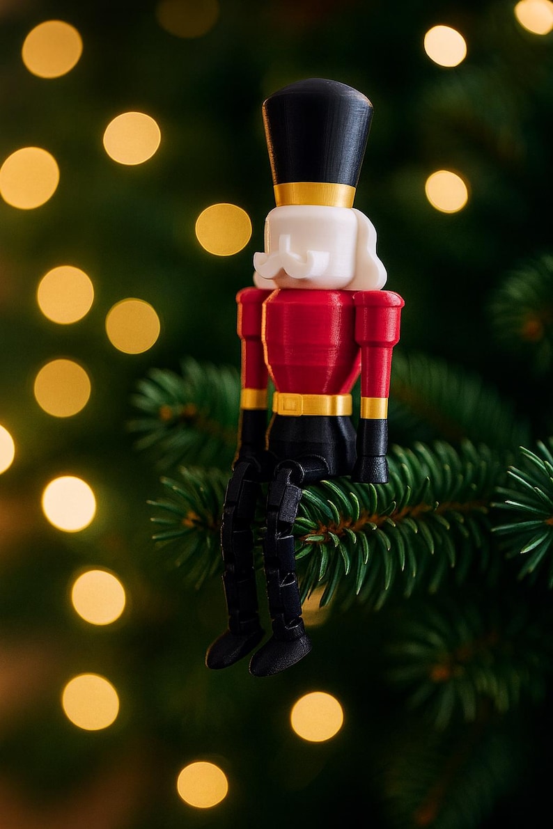 K&ouml;nnte beinhalten: Ein dekorativer Weihnachtsschmuck in Form eines Spielzeugsoldaten. Er hat einen schwarzen Hut, wei&szlig;es Haar und eine rote Jacke mit goldenen Verzierungen und schwarzen Beinen. Der Schmuck sitzt auf einem gr&uuml;nen Kiefernzweig, mit verschwommenen gelben Lichtern im Hintergrund.