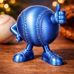 Puede incluir: Una figura azul en forma de pelota de béisbol con brazos, piernas y zapatos, haciendo un gesto de pulgar hacia arriba. El béisbol tiene costuras visibles y está sobre una superficie de madera. Hay otra pelota de béisbol en el fondo.