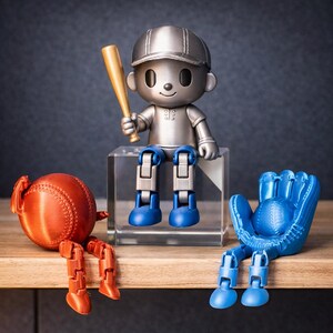 May include: A silver-colored articulated figure wearing a cap and holding a gold baseball bat sits on a clear block. To the left, an orange baseball-shaped figure with articulated legs. To the right, a blue baseball glove figure with legs.