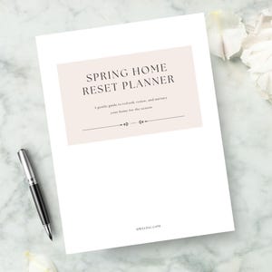 May include: A white paper with the text "SPRING HOME RESET PLANNER" in a light brown box, with a pen and flowers. The planner includes the text "A gentle guide to refresh, renew, and nurture your home for the season."