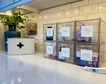 May include: Clear plastic storage containers with labels for various medications and first aid supplies. The labels include "Eye & Ear", "Ointments", "Vitamins", "Pain Reliever", "Digestion", and "Band-Aids".