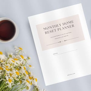 May include: A flat lay featuring a white mug filled with dark liquid, a bouquet of daisies, a pen, and a planner. The planner has the text "MONTHLY HOME RESET PLANNER" in a light brown box. The background is a light blue surface.