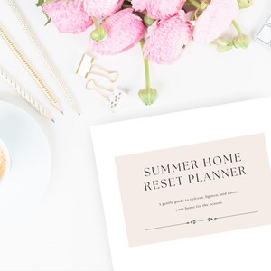 Könnte beinhalten: Draufsicht mit einer weißen Tastatur, Bleistiften und einer Kaffeetasse. Ein Planer mit dem Text "Summer Home Reset Planner" steht im Mittelpunkt. Rosa Blumen und goldene Büroklammern sorgen für Farbe.