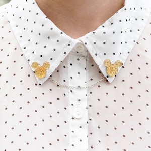 May include: A white collared shirt with black polka dots and two gold Mickey Mouse pins on the collar.