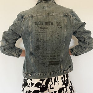 May include: A blue denim jacket with a black print on the back that says "Date Nite at Disneyland" with a cartoon image of a character holding a cup. The text also says "Every Friday and Saturday Night Open till 12 MIDNIGHT Disneyland."