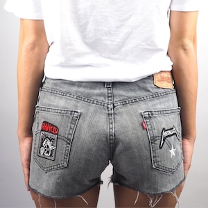 May include: Gray denim shorts with frayed edges and two band patches. The left patch is red and white and says "Rancid". The right patch is black and white and says "Metallica".