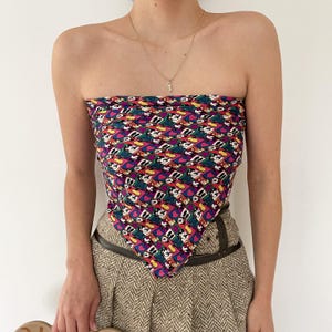May include: A colorful strapless top with a repeating pattern of Mickey Mouse. The top features a vibrant mix of colors including purple, pink, green, and yellow. The top is paired with a brown belt and a patterned skirt.