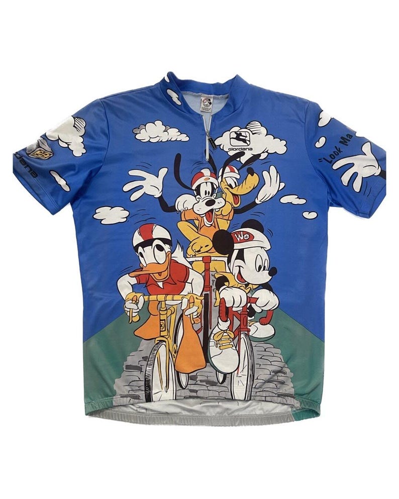 May include: A blue cycling jersey with a print of Mickey Mouse, Donald Duck, Goofy, and Pluto riding bicycles. The jersey has a zipper and the text "Look Ma" on the right sleeve.
