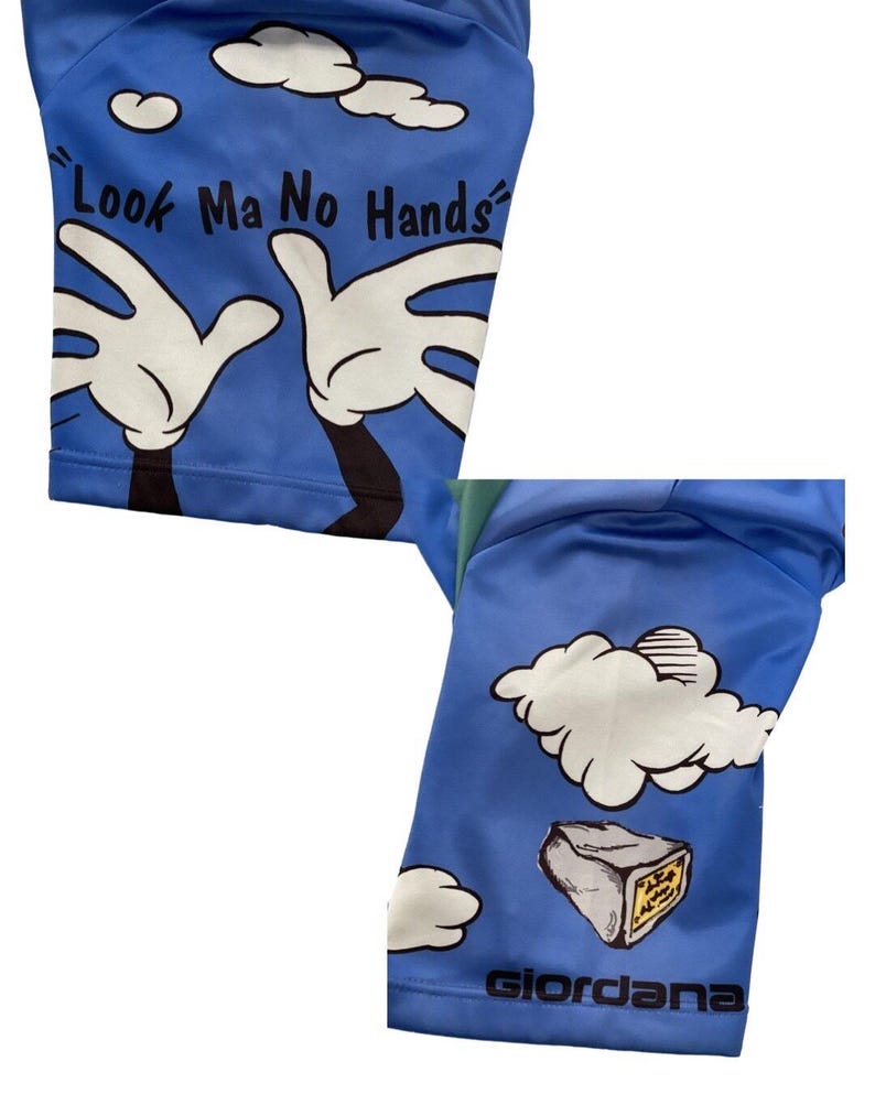 May include: Blue cycling shorts with a cartoon design of hands reaching up to a cloud with the text "Look Ma No Hands". The shorts have a white cloud and a gray rock with the word "Giordana" printed on the bottom.