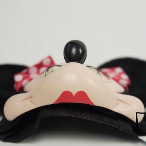 Pu&ograve; includere: Cappellino da baseball nero con un design di Minnie Mouse. Il cappello ha una visiera nera, una corona nera e un viso di Minnie Mouse con labbra rosse, occhi neri e un naso nero. Il cappello ha anche un fiocco rosso con pois bianchi sul lato.