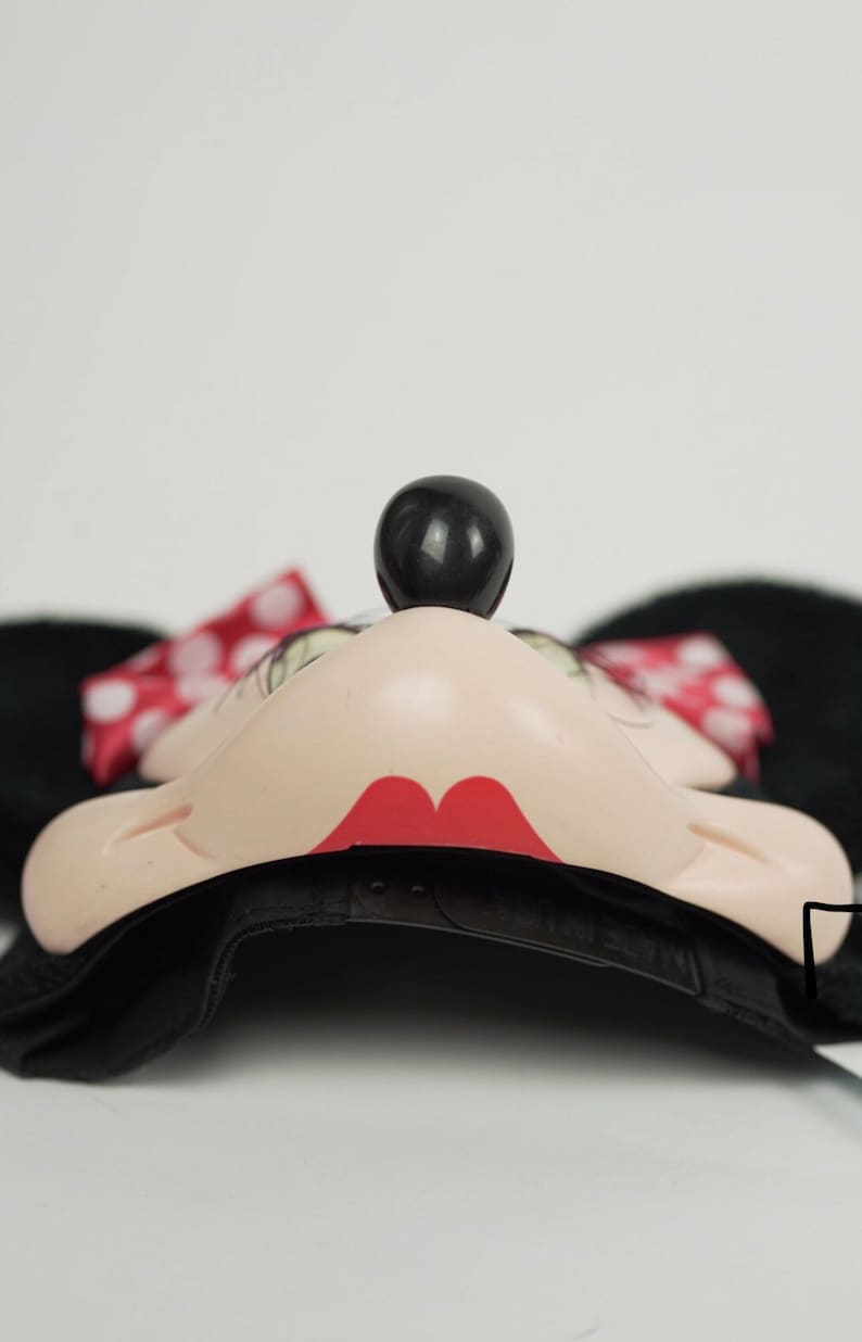 Pu&ograve; includere: Cappellino da baseball nero con un design di Minnie Mouse. Il cappello ha una visiera nera, una corona nera e un viso di Minnie Mouse con labbra rosse, occhi neri e un naso nero. Il cappello ha anche un fiocco rosso con pois bianchi sul lato.