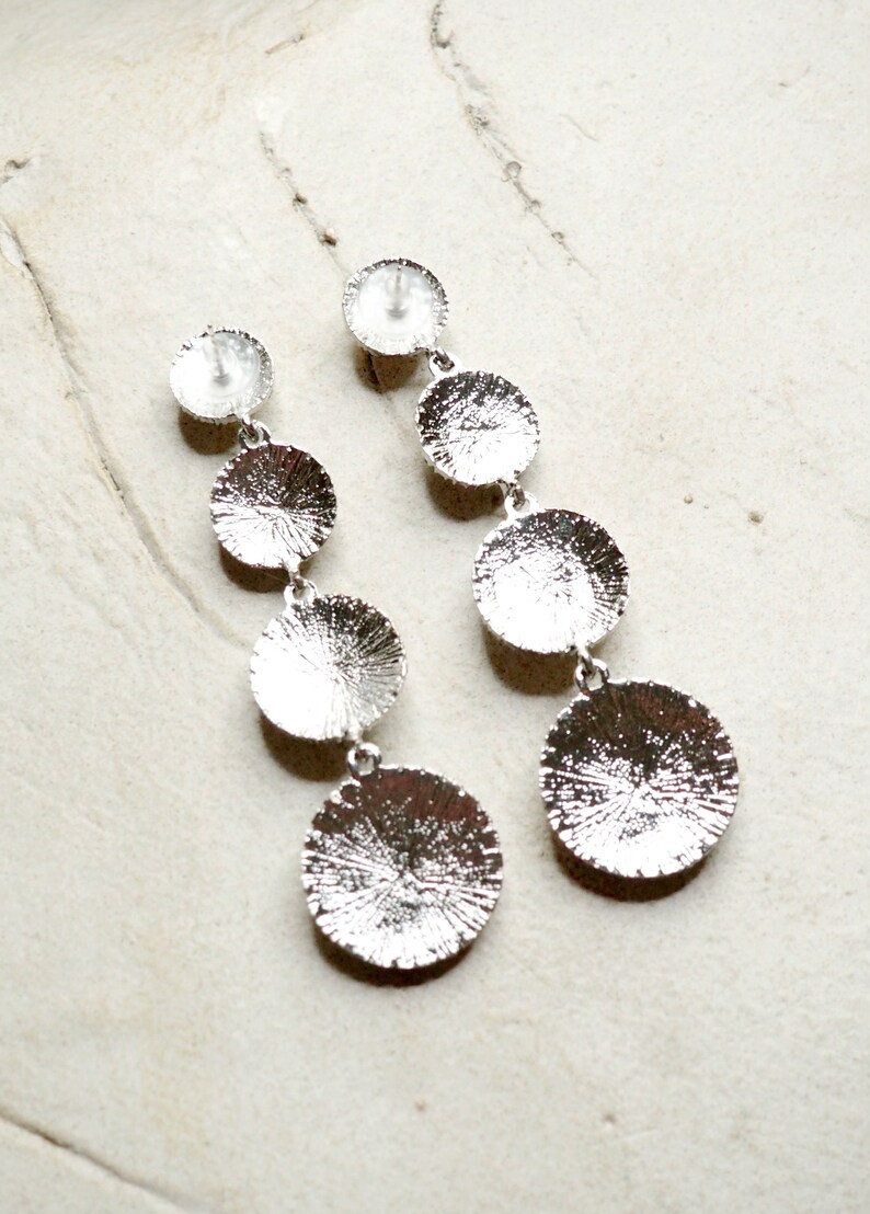 May include: Silver dangle earrings with four round discs of varying sizes. The discs have a textured surface.